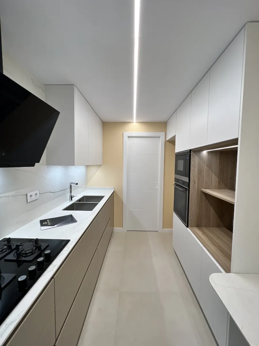Cocina vista desde el lavadero: Espacio de cocina optimizado con muebles a medida de alta calidad y acabados premium en la calle Valencia.