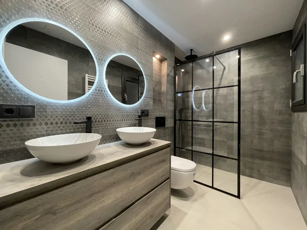 Detalle del mueble suspendido acabado madera y mampara de ducha con perfilería negra en esta reforma integral de piso en Horta-Guinardó.