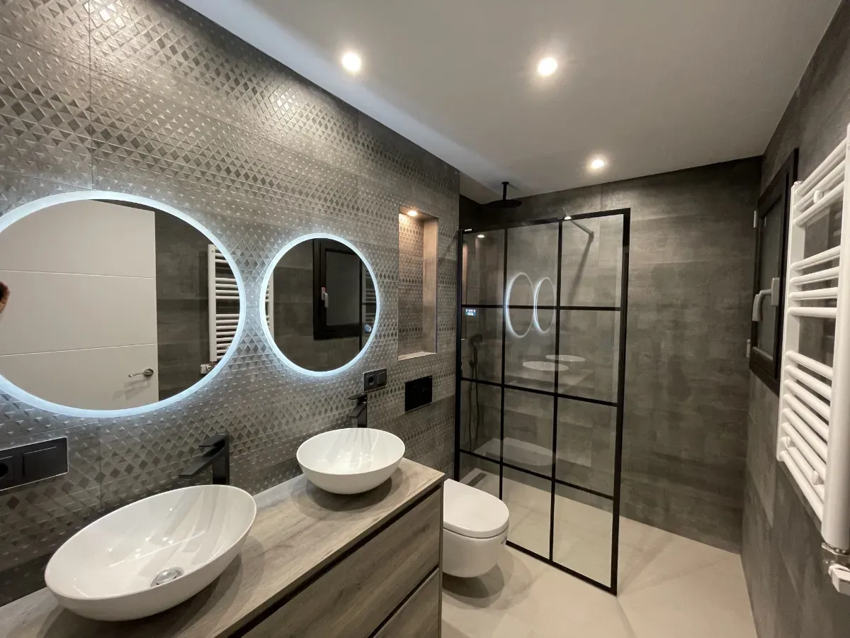 Cuarto de baño moderno con revestimiento texturizado, sanitarios suspendidos y grifería negra mate.