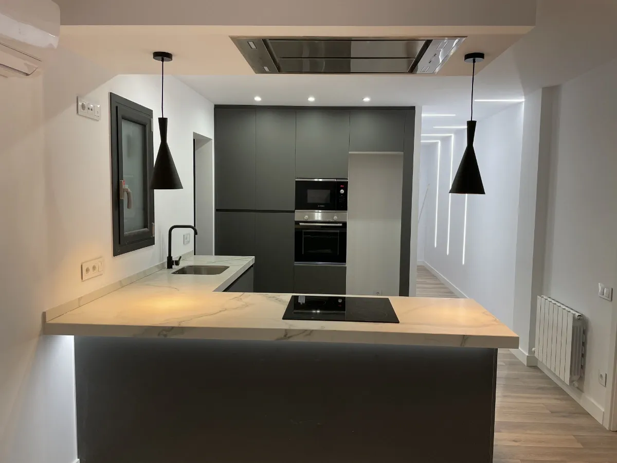 reforma integral de piso en Horta Guinardó - Calle Granollers - Barcelona - detalle de cocina abierta con su peninsula y extractor moderno, pasillo al fondo con excelente iluminación LED