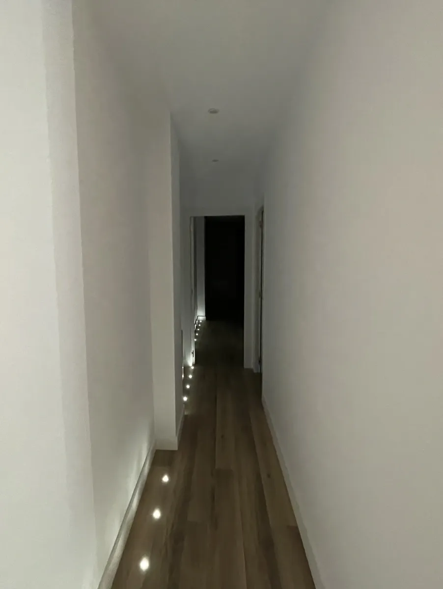 Pasillo moderno con iluminación LED rasante a nivel del suelo de madera laminada en esta reforma completa de vivienda.