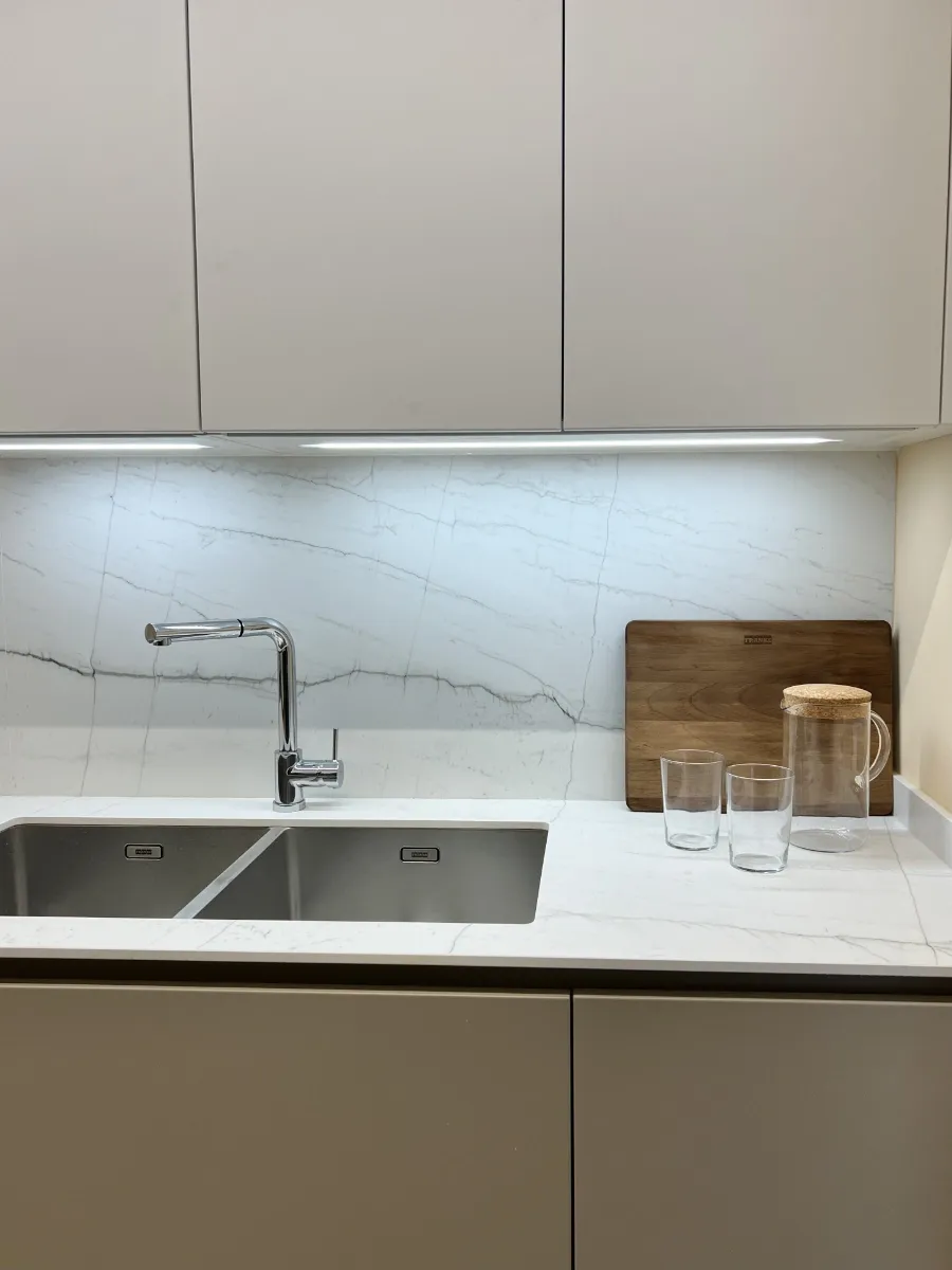 Detalle fregadero y Silestone: Fregadero doble de acero inoxidable y frontal protector de Silestone iluminado con LED bajo muebles de cocina modernos y funcionales.