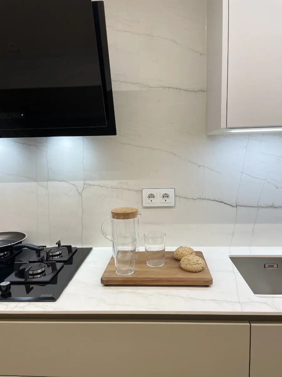 Detalle fogones y campana: Placa de gas tradicional y campana decorativa negra perfectamente integradas en el diseño de esta reforma integral de piso en L'Eixample.