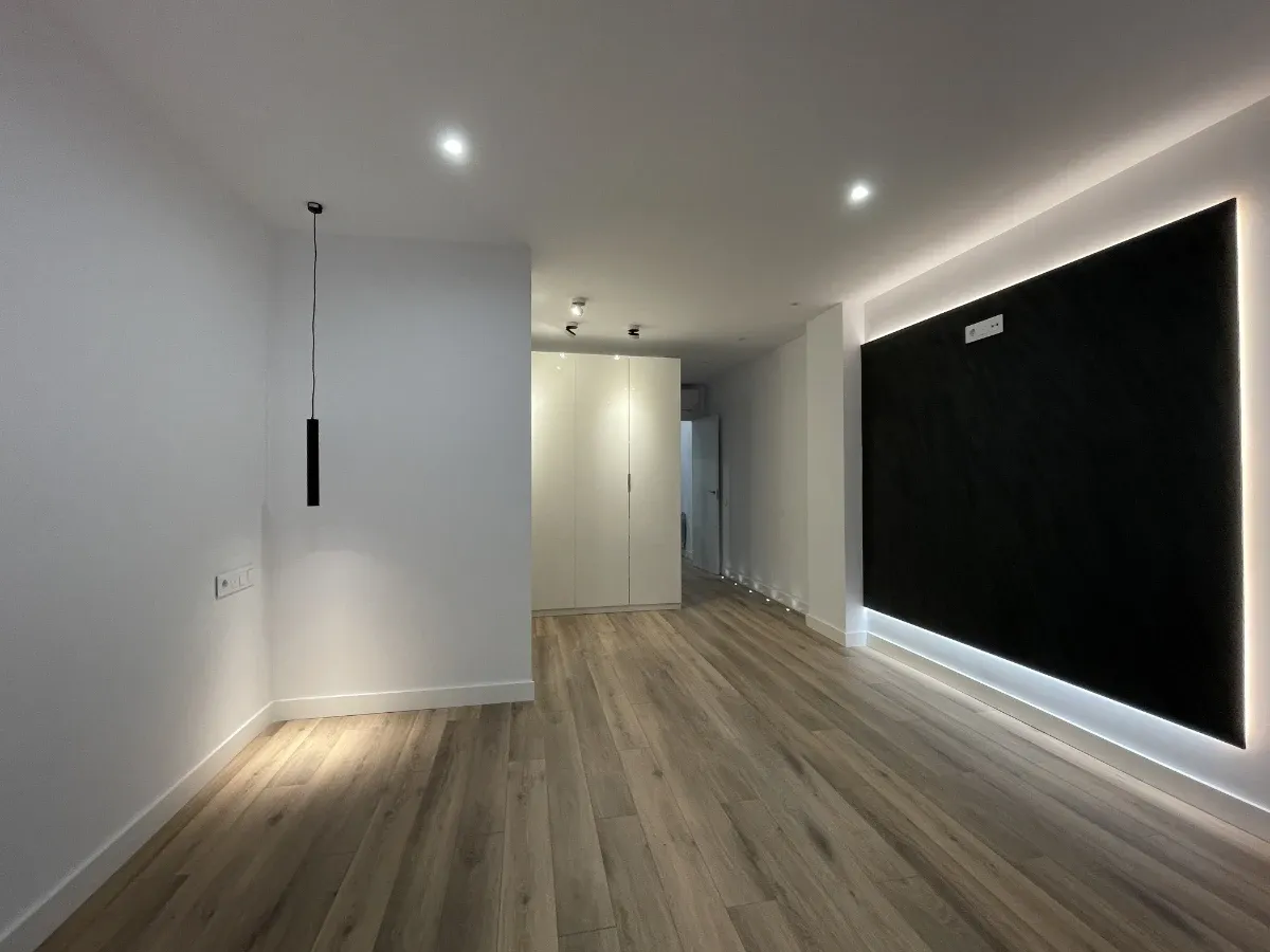 Amplia habitación con armario empotrado blanco, suelo laminado y panel para home cinema tras una reforma integral de piso en Horta-Guinardó.