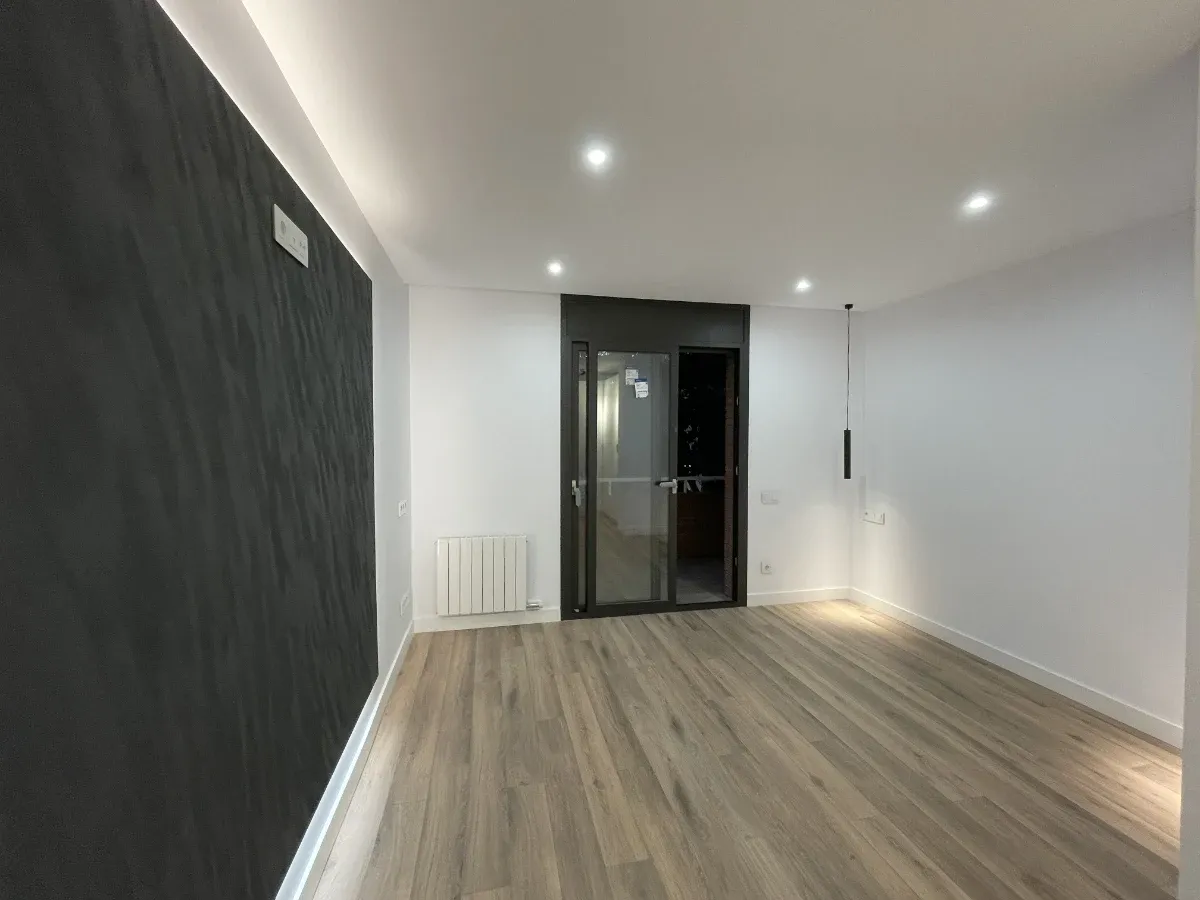 Habitación luminosa con acceso a balcón y carpintería metálica oscura, resultado de una reforma completa de vivienda en Barcelona.