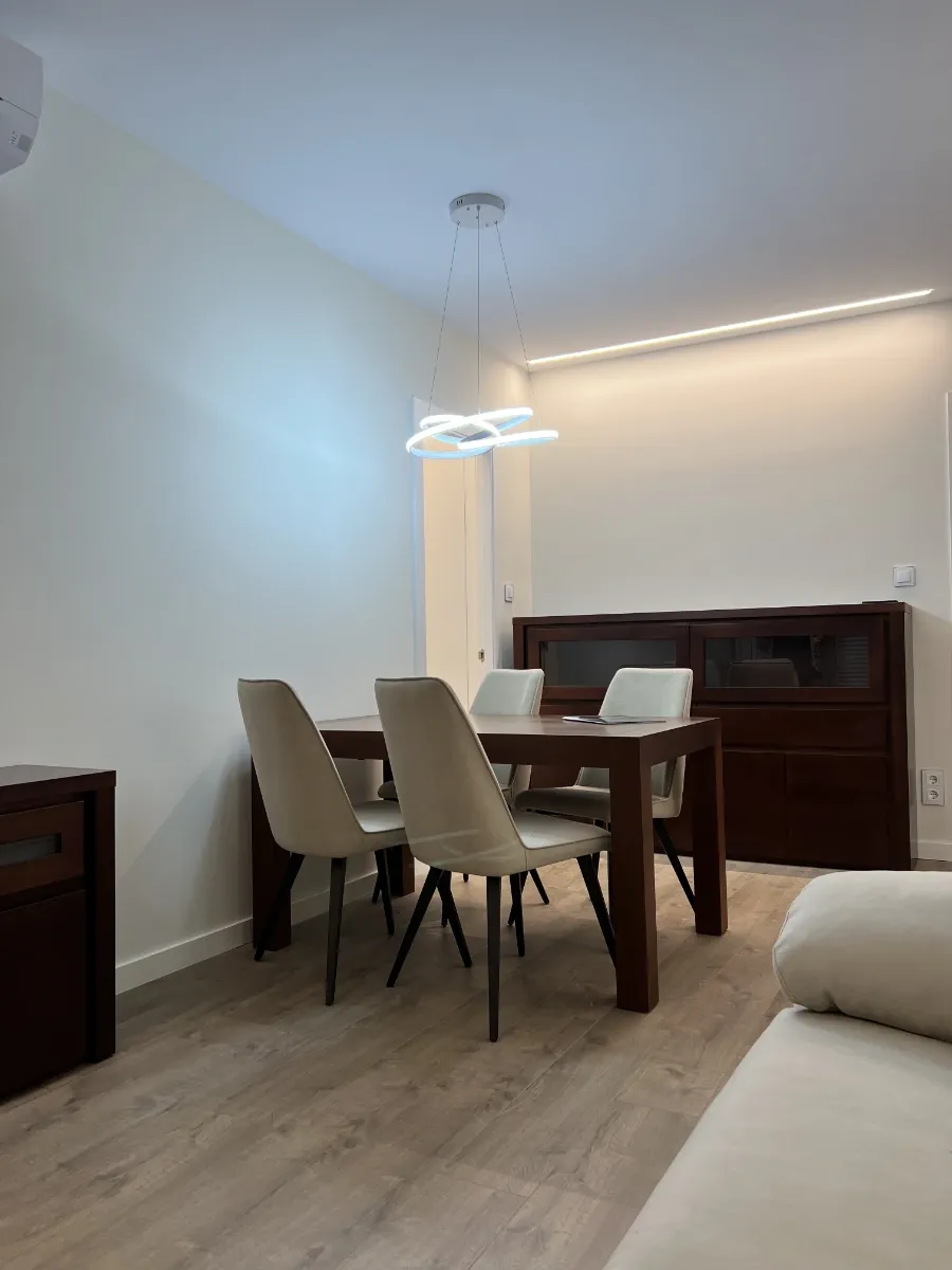 Reforma integral de piso en l' Eixample: Salón comedor general: Vista del salón comedor con suelo de madera y mobiliario elegante tras una reforma integral de piso en L'Eixample