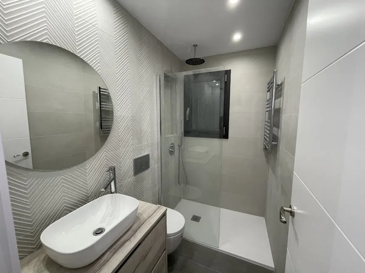 Detalle del baño de invitados con espejo circular y acabados de alta calidad, un ejemplo de nuestros proyectos de interiorismo.