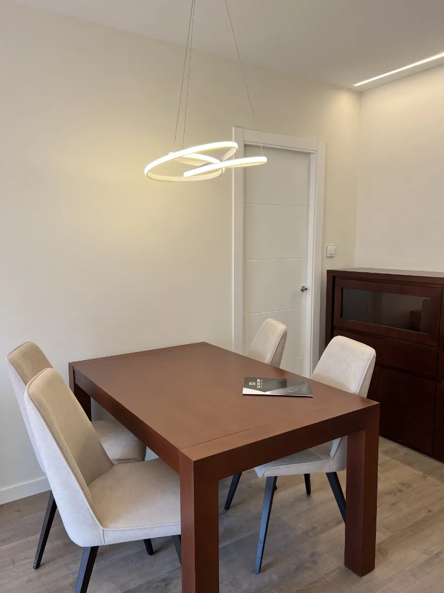 Salón comedor detalle mesa: Detalle de la mesa de comedor de madera oscura y lámpara LED de diseño en nuestro proyecto de reforma llave en mano en Barcelona.