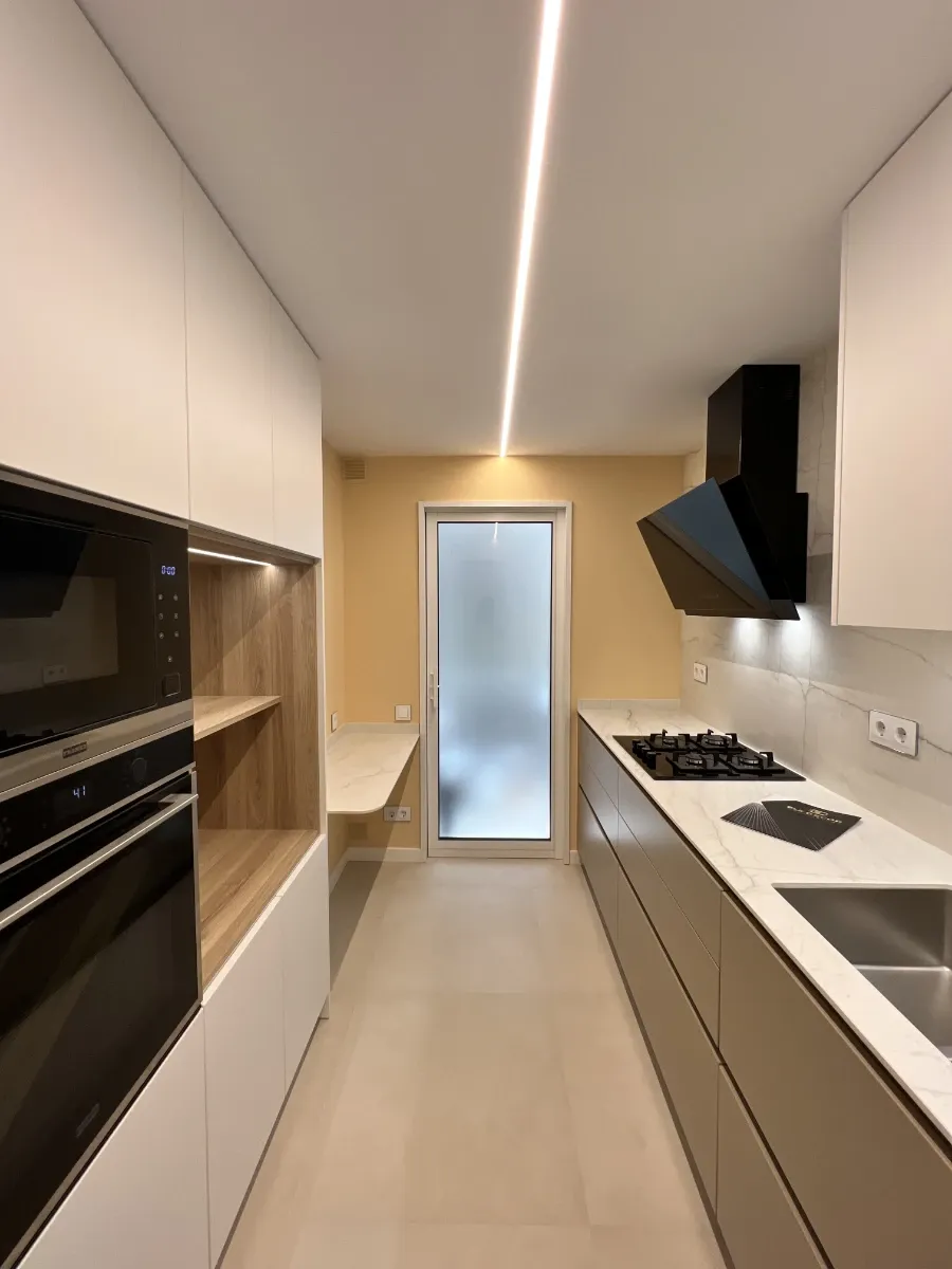 Cocina vista desde la entrada: Cocina alargada con perfil de iluminación LED en el techo y acceso al lavadero, un excelente ejemplo de proyecto de reforma llave en mano.
